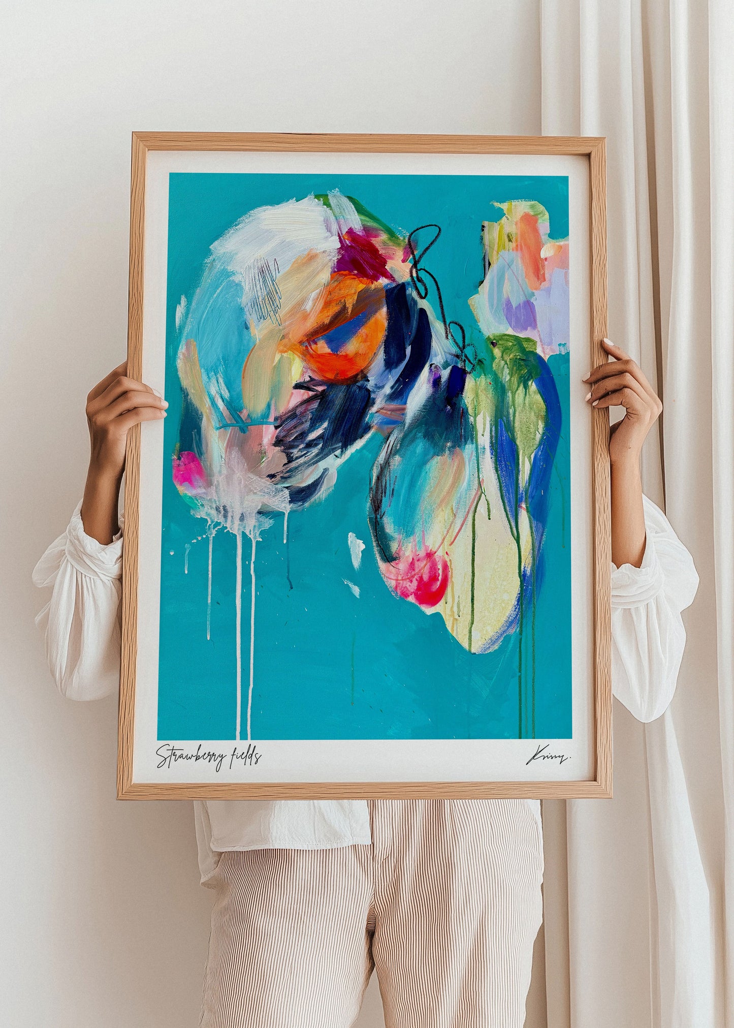 Person holding a colorful abstract painting in a wooden frame against a white wall.